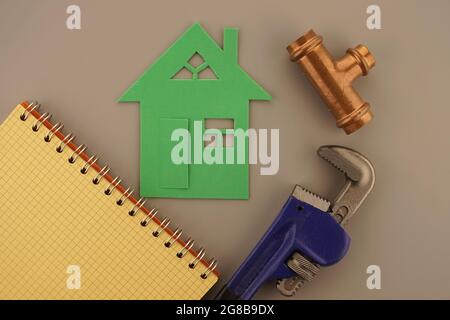 DIY, renovation or new build home concept with wrench, copper plumbing joint and notebook alongside a spiral bound notebook and green cutout of a hous Stock Photo