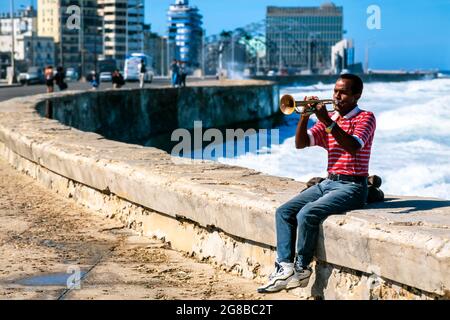 Young Cuban man playing trumpet on Malecon wall with sea and city in background, Havana, Cuba Stock Photo