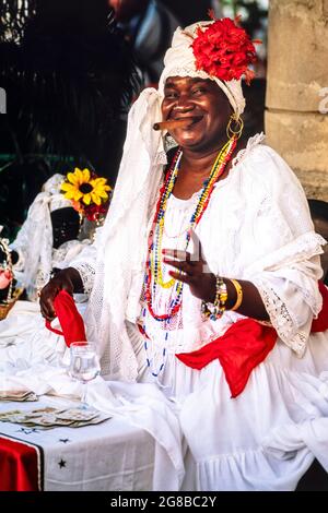 Ethnic Cuban fortune teller smoking a cigar and smiling in front of table with playing cards, Havana, Cuba Stock Photo