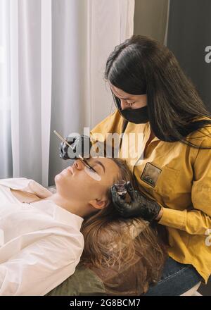 Woman on cosmetic procedure at salon. A girl in a beauty salon on the procedure of coloring her eyelashes. Care for eyebrows and eyelashes. Stock Photo