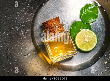 Packshot of Bergamot essential oil in a glass bottle with cork, fresh bergamot fruit, and green leaf on stainless steel with water drops background. B Stock Photo