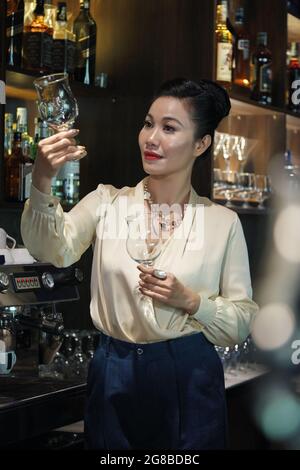 Elegant female restaurant owner checking wine glasses in bar Stock Photo