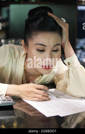 Tired restaurant manager leaning on bar counter and analyzing data in sales reports Stock Photo