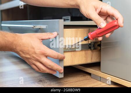 Young Handyman In Overall Installing Drawer In Kitchen. The man adjusts the drawer. Self-assembly of furniture. Stock Photo