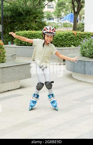 Portrait of little girl in special equipment smiling at camera while skating outdoors in the city Stock Photo