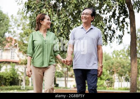 Cheerful senior couple holding hands when walking outdoors in city park having romantic date Stock Photo