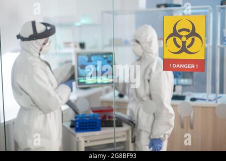 Danger zone sign in medical laboratory and scientist working dressed in ppe suit. Group of doctors examining vaccine evolution using high tech for diagnosis against covid19. Stock Photo