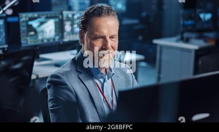 Portrait of Positive Professional Technical Controller Sitting at His Desk with Multiple Computer Displays Before Him. In the Background His Stock Photo
