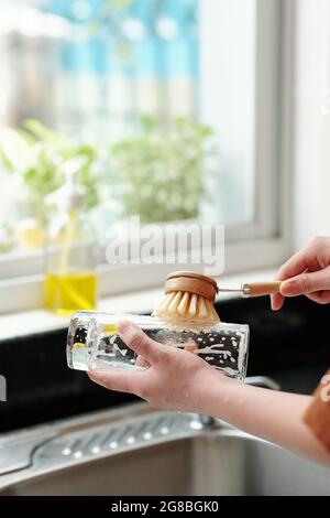 Hands of young woman washing dishes with dishwashing liquid and brush Stock Photo
