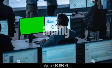 Green Screen Horizontal Mock Up on a Computer Display Used by a Male Trade Specialist. Team of Brokers and Finance Specialists Sit in Front of Stock Photo