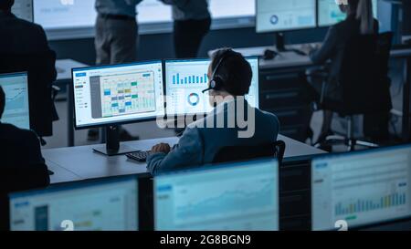 Professional Male Trade Specialist is Working on a Computer with Big Data in Modern Monitoring Office. Employees Sit in Front of Displays with Stock Photo