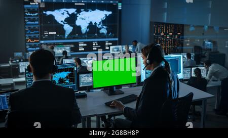 Green Screen Horizontal Mock Up on a Computer Display Used by a Female Technical Client Support Specialist Wearing Headset. Team of Engineers Work in Stock Photo