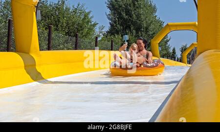 Women with daughter having fun water sliding on balloon in Ogre city Aquapark Water Slide, Latvia Stock Photo