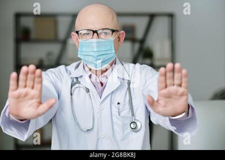 Portrait of mature doctor in protective mask showing his clean hands during his work at hospital Stock Photo