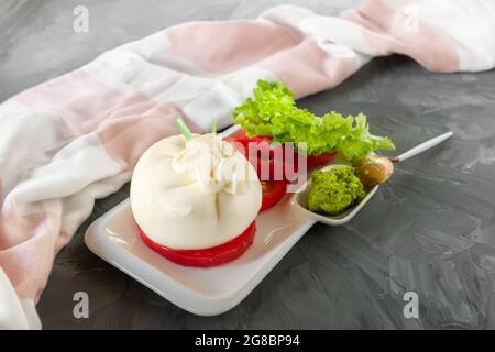Fresh soft cream burrata cheese with tomatoes, green salad and pesto sauce on a beautiful white plate. Stock Photo