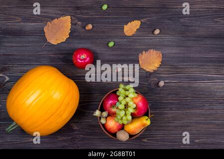 Orange pumpkins with apples and pears in a basket with grapes, nuts and leaves on a brown wooden table. View from above Stock Photo