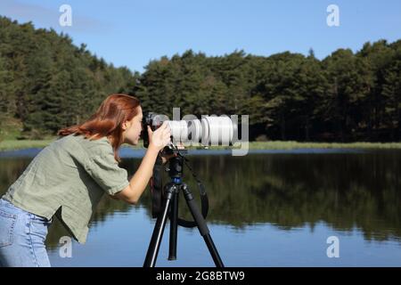 Side view portrait of a photographer taking photo with telephoto and dslr camera in a lake Stock Photo
