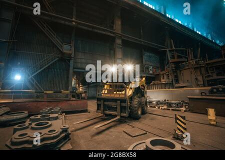 Small loading tractor or mower at work in metallurgical factory workshop. Stock Photo