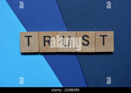 Trust, word in wooden alphabet letters on blue background Stock Photo