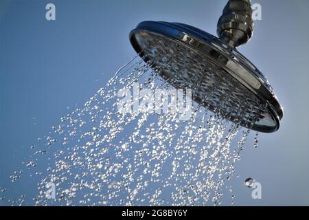 A shiny, metal shower head spraying out water droplets against a blue background Stock Photo