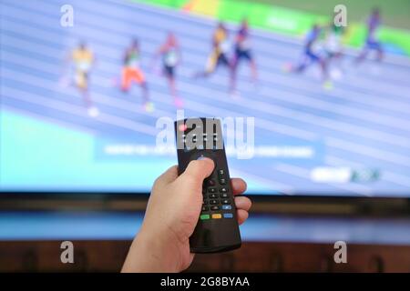 Watching sports track and field program on tv. Close up on remote control. Stock Photo