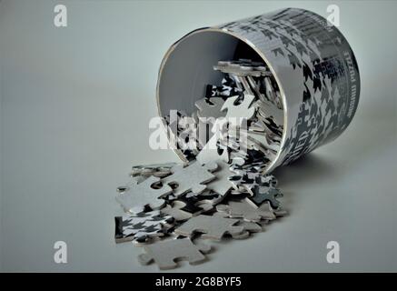 Black and white puzzle pieces fall out of their round box and are scattered Stock Photo