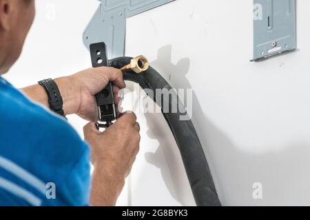 Technician installing indoor air conditioner compressor condenser copper pipe on wall Stock Photo