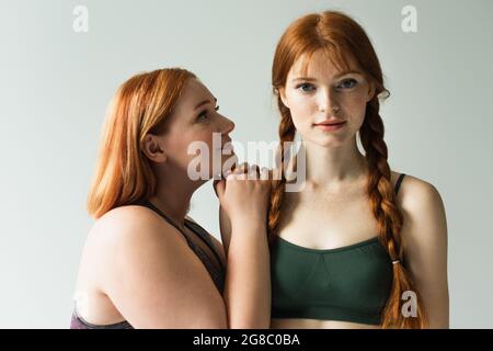 Plus size sportswoman looking at redhead friend isolated on grey Stock Photo
