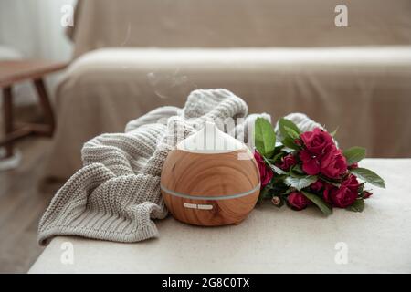 Modern oil aroma diffuser in the living room on the table with knitted element and flowers. Stock Photo