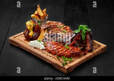 Grilled assorted meat platter with potato wedges and sauces Stock Photo