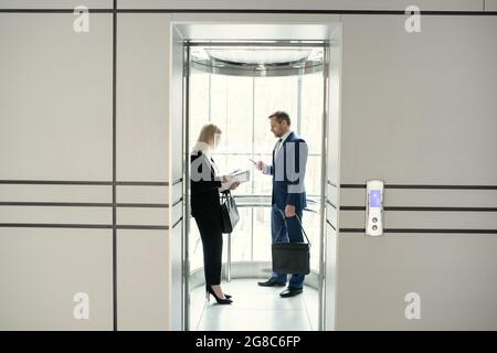 Two business people standing in elevator of modern office building Stock Photo