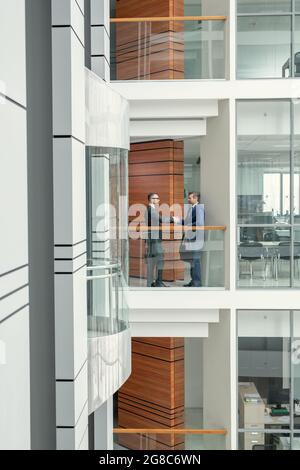 Two business men in suits shaking hands and greeting each other while standing at office corridor Stock Photo