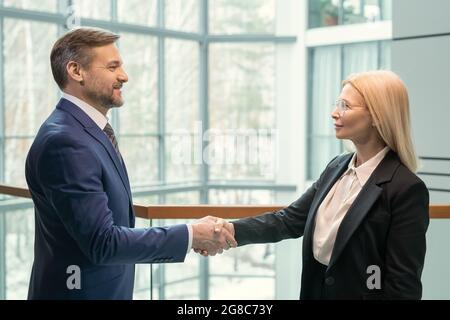 Side view of business partners looking at each other and shaking hands, they greeting each other at office Stock Photo