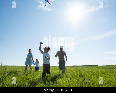 Parents and children running with kite on summer holiday vacation, perfect meadow and sky on seaside Stock Photo
