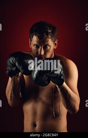 This is a dramatic portrait of a boxer in old boxing gloves on a dark background. An athletic mixed martial arts fighter stands in a fighting stance. Banner for sports events. Stock Photo