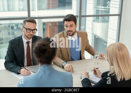 Young businessman talking to his partners while they sitting at the table and discussing new contract during business meeting at board room Stock Photo