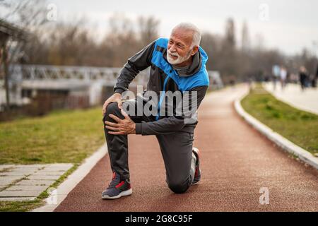 Active senior man is having pain in knee while jogging. Stock Photo