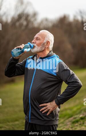 Senior man is drinking water after exercising in park. Stock Photo