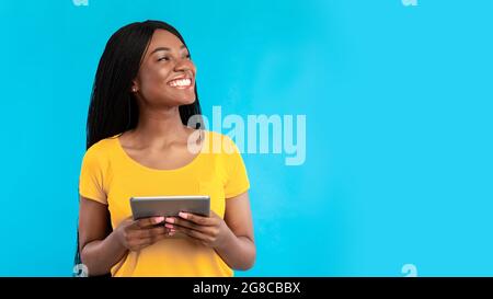 Black woman using digital tablet looking aside over blue background Stock Photo