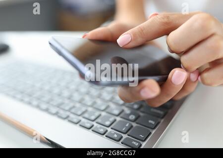 Girl presses finger on screen of smartphone on table is laptop Stock Photo