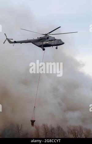 Firefighter helicopter with a water tank in smoke from a fire. Trees in the smoke of a fire. Stock Photo