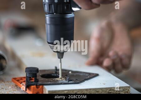 Screwing a self-tapping screw into a metal fastening hole on a wood strip using a screwdriver, the work of a carpenter. Stock Photo
