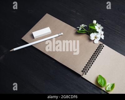 Photo of blank kraft notebook, pencil, eraser and spring flowers on wood table background. Stock Photo