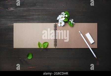 Photo of blank kraft sketchbook, pencil, eraser and spring flowers on wooden background. Template for placing your design. Flat lay. Stock Photo