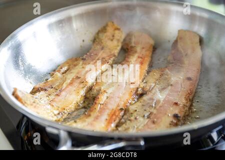 Frying bacon in stainless steel frying pan on stove top Stock Photo - Alamy