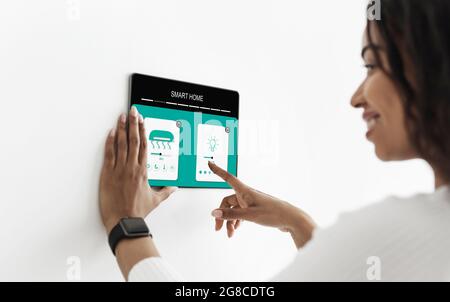 Woman controlling smart home with digital touch screen panel installed on white wall in living room Stock Photo