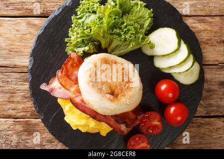 Hot breakfast of English muffin with scrambled eggs, bacon, cheese and vegetables close-up on a slate board on the table. horizontal top view from abo Stock Photo