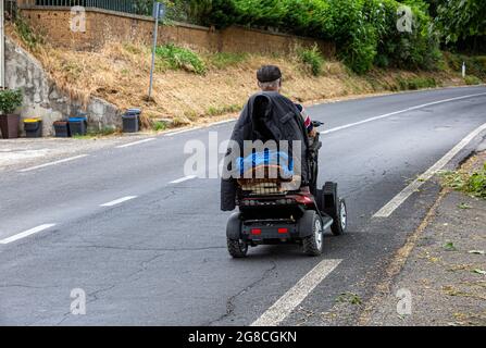 Elderly man driving a disability scooter on a rural road. Stock Photo