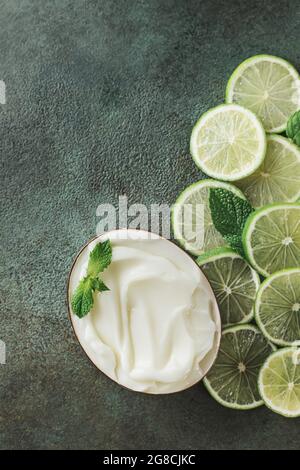 Jar with cosmetic product with lime and mint halves on green concrete. Natural citrus cosmetics with vitamin C. Copy space. Stock Photo