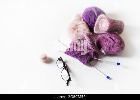 Knitting threads, knitting needles and glasses on white table background. Stock Photo